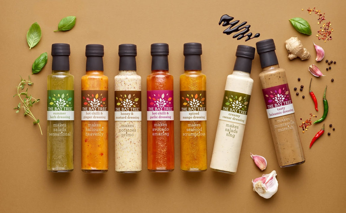 Row of various bottles of 'The Bay Tree' products on a brown background with ingredients.